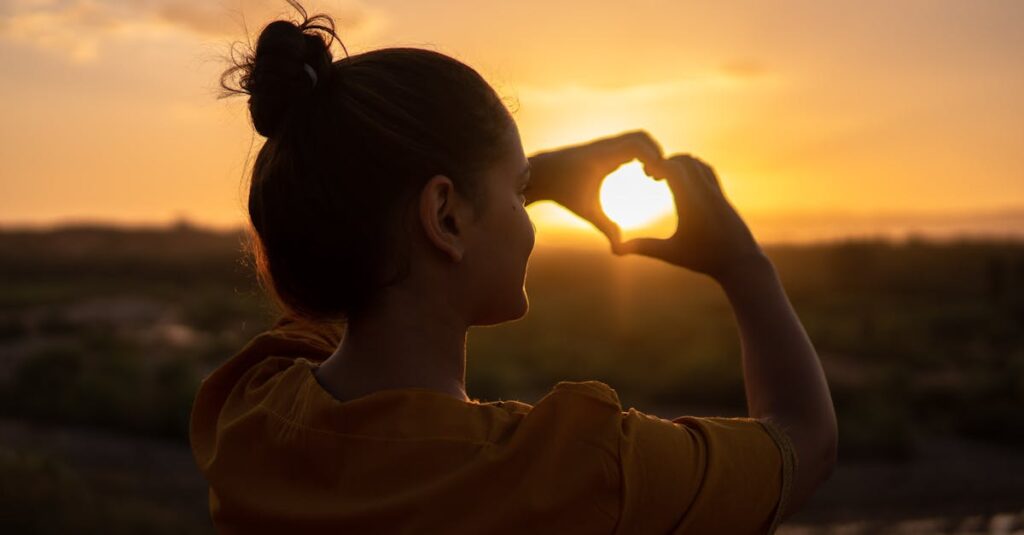 A silhouette of a young woman forming a heart shape at sunset in Kelâat M
