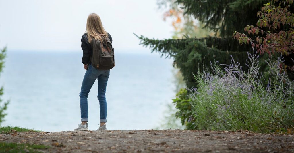 A young woman with a backpack stands on a scenic nature path overlooking a lake.