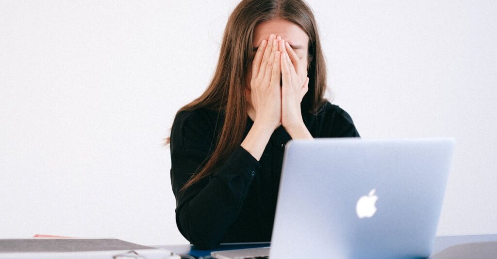 Woman feeling stressed and overwhelmed at her desk while working remotely on a laptop.